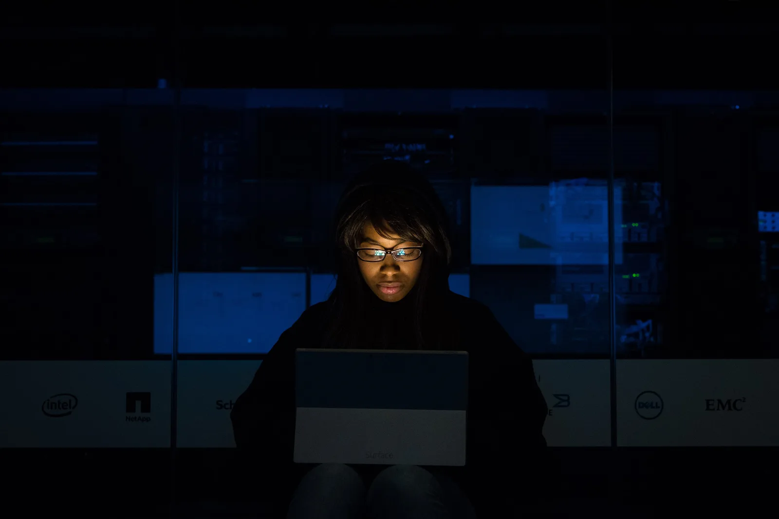 A woman deeply engrossed in programming on a laptop at night in a data center.