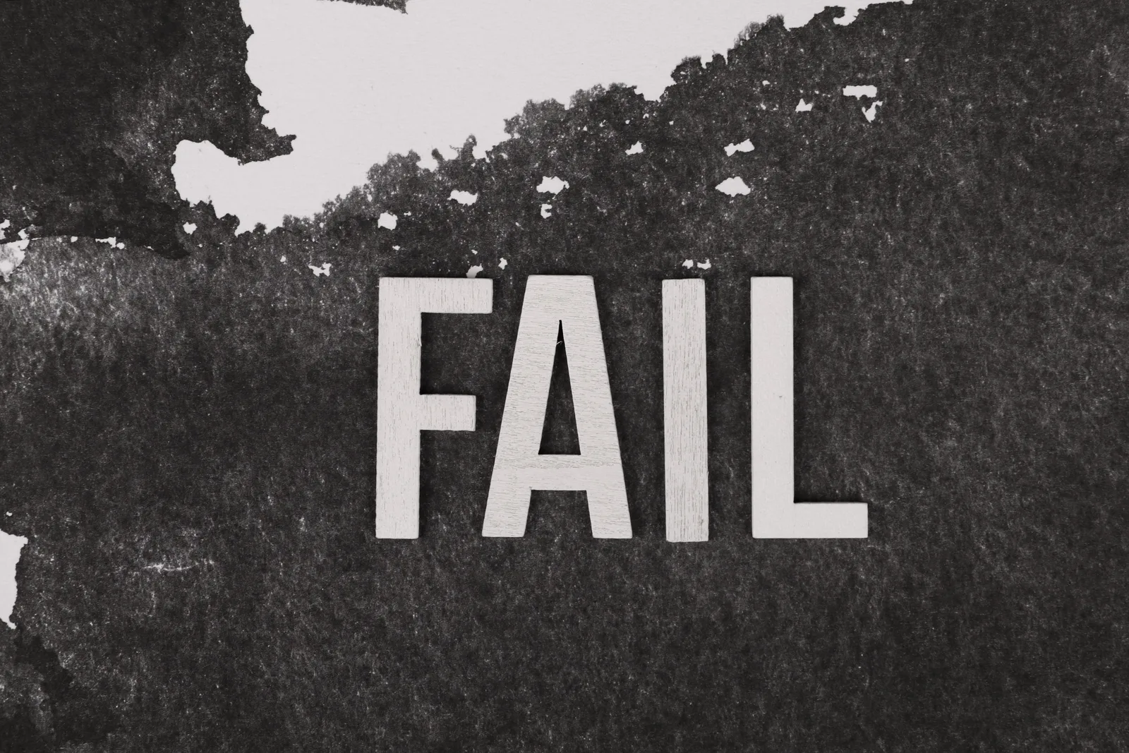 Grayscale image of the word 'FAIL' on a textured, monochrome background.