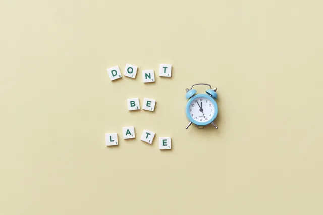 Flat lay of a blue alarm clock and letter tiles spelling 'Don't Be Late'. Unbeantwortete Freigaben zeitlich begrenzen